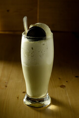 A glass of milk with a small cake on a wooden table 