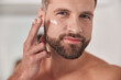 © Friends Stock - Attractive mature man applies cream onto skin under eye in bathroom