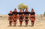Fototapeta Sawanna - Group of women of the Himba tribe are walking through the desert in national clothes.