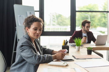 Wall Mural - African american businesswoman looking at calculator near smartphone and documents in office