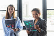 © LIGHTFIELD STUDIOS - Smiling african american businesswoman looking at paper with charts near young colleague in office