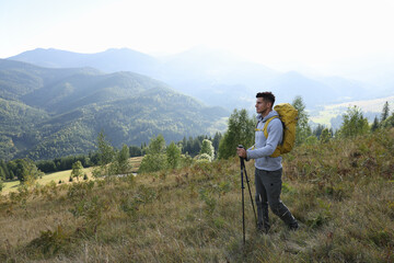 Canvas Print - Tourist with backpack and trekking poles hiking through mountains, space for text