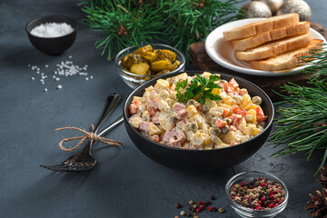 Wall Mural - Olivier salad in a black bowl on a dark background with pine branches.