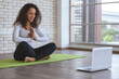 © amornchaijj - Beautiful young black slim woman live streaming training or learning yoga with laptop in bedroom. Stay at home and self-quarantine in spread of coronavirus covid-19