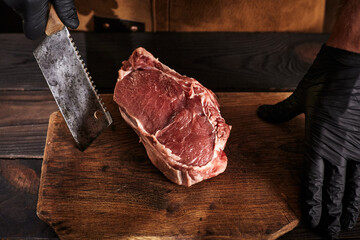 A butcher with a cleaver in black gloves and a leather apron holds a piece of meat.