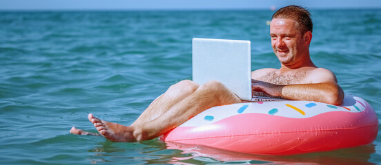 Work from anywhere and remote occupation concept. Hupy businessman freelancer working with laptop computer on inflatable ring in Tropical sea. Copy space. Horizontal image.