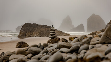 Wall Mural - Stack of pebbles on sand in a foggy ocean side, horizontal background