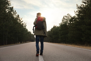 Wall Mural - Man with backpack going along road near forest, back view