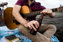 Anonymous Guitarist Opening Beer While Sitting On Beach