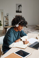 vertical portrait of african-american teenage boy studying at home or in college dorm and using lapt