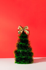 Wall Mural - Minimal composition of green Christmas tree with golden bow on pastel red background. New Year concept. Copy space.