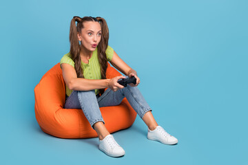 Wall Mural - Full length photo of funky young brunette lady sit on chair play station wear jeans t-shirt sneakers isolated on blue color background