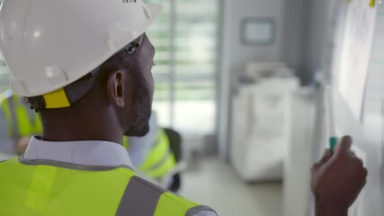 Wall Mural - Back view of mixed-race engineer in hardhat and vest writing on board at corporate meeting