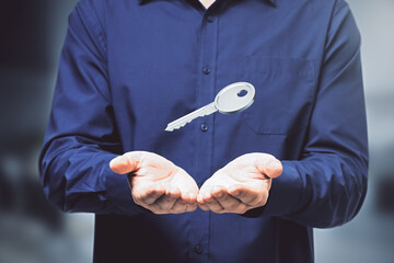 Poster - Close up of male hands holding silver key on blurry background. Mortgage and purchase concept.