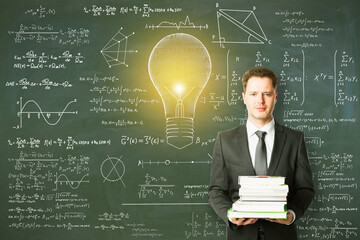 Wall Mural - Attractive young european businessman holding books with abstract lamp sketch with mathematical formulas on chalkboard/blackboard wall background. 