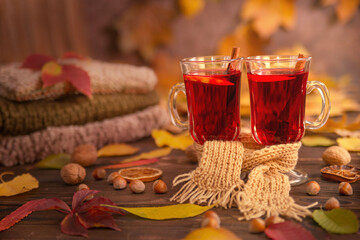 Autumn, fall leaves, two glasses of hot wine, wrapped in one scarf on the background of a wooden table. A seasonal drink, a relaxing Sunday and the concept of warmth, care and love.