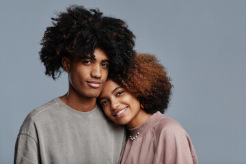 Wall Mural - Minimal portrait of young African-American couple with natural curly hair smiling at camera against blue background, copy space