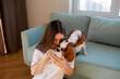 Young woman sitting at home with Cavalier King Charles Spaniel dog and phone.