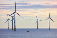 Small Fishing Boat Dwarfed By Huge Wind Turbines Off The North East Coast, Redcar, North Yorkshire, England, UK.
