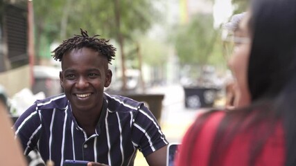 Wall Mural - Two male multi ethnic diverse friends enjoying conversation in a outdoors city restaurant bar. Handsome Latin man with make up on his face together with trendy African guy