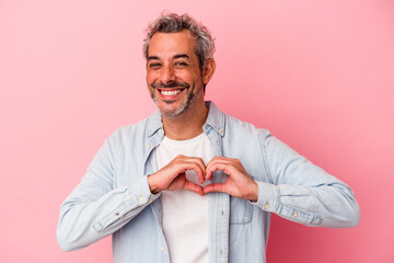 Middle age caucasian man isolated on pink background  smiling and showing a heart shape with hands.