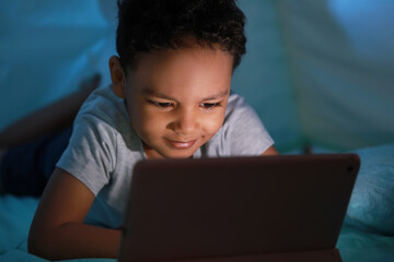 Poster - Little African-American boy watching cartoons on tablet computer in play tent at night