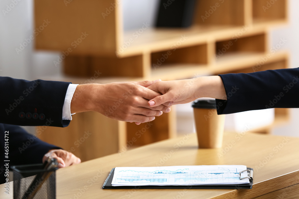 Business partners shaking hands at table in office, closeup