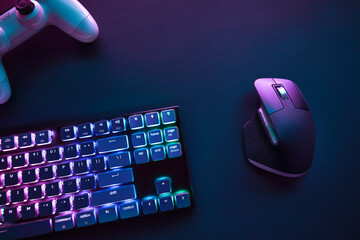 Top down view of color backlighted computer keyboard, mouse and game controller on desk.