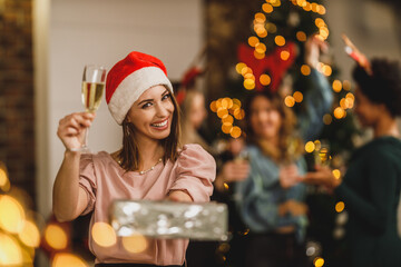 Sticker - Woman Making Toast With Champagne And Holding Gift As They Celebrate Christmas At Home Party