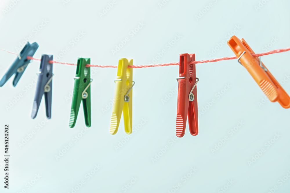 Many plastic clothespins hanging on rope against blue background, closeup