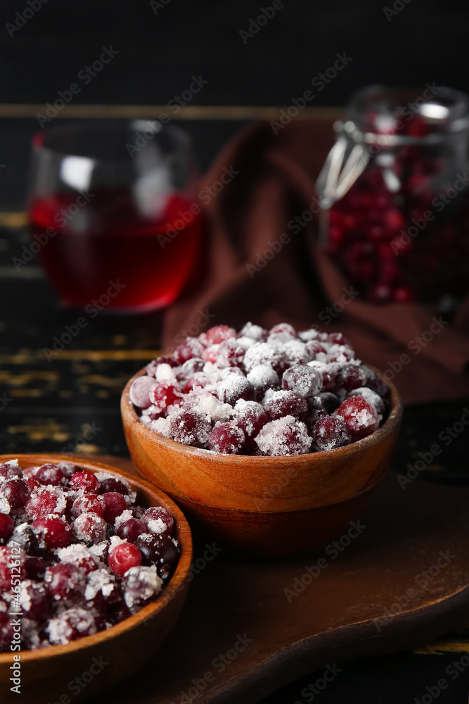 Bowls with tasty sugared cranberries on black wooden background