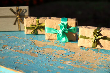 Wall Mural - Four, 4 wrapped vintage gift boxes with olive silk ribbon bow on blue (turquoise) old wooden background. Present box in craft paper with green bow with shadow. Holiday concept. Selective focus