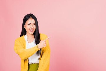 Wall Mural - Asian happy portrait beautiful cute young woman standing makes gesture one fingers point upwards above presenting product something, studio shot isolated on pink background with copy space