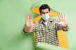 © Drobot Dean - Man wearing face mask gesturing while posing into hole in green background