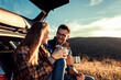 © Zoran Zeremski - Couple on road trip sitting in trunk of a car resting and drinking coffee.