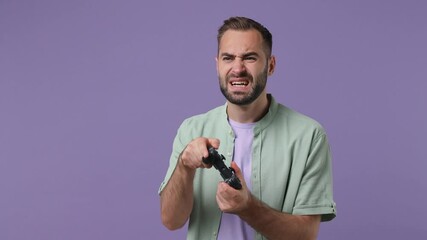 Canvas Print - Gambling attractive charming happy passionate young bearded man 20s years old wears mint shirt hold in hand play pc game with joystick console isolated on plain light purple background studio portrait