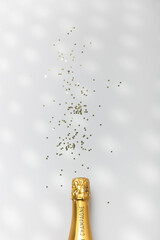 Bottle of champagne and confetti on white background, top view.