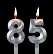 Burning silver birthday candle isolated on black background, number 85
