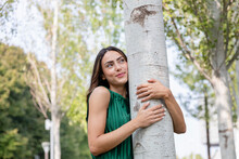 Smiling Young Woman Hugging Tree At Park