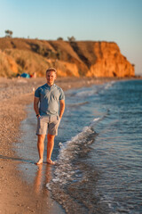 Attractive young man walks on the beach at sunset by the sea. The concept of an active lifestyle and summer holidays