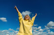 © Westend61 - Smiling mid adult woman standing with arms raised under cloudy sky