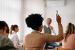 © Drazen - Rear view of black student raises her hand to answer question during class at lecture hall.