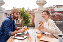Smiling Woman Showing Smartphone Screen To Friend Siting At Table