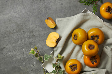 Wall Mural - Front view of circleTop view of a light blue napkin of persimmon , green leaf in grey background for food advertising  , square podium 