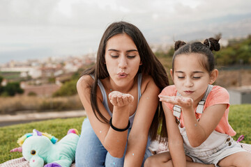 Wall Mural - Teenage girl having playful time with little sister in city park while blowing glitter stars