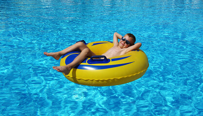 Wall Mural - Boy relaxing on the inflatable ring in swimming pool.