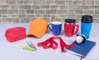 Composition of different promo products with rich colors -Thermo mugs, Lanyards Neck Strap, pens, mug, silver table office clock, zipped coin purse fabric, notebook,cap On desk grey 