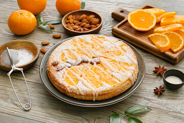 Plate with tasty orange pie and ingredients on wooden background