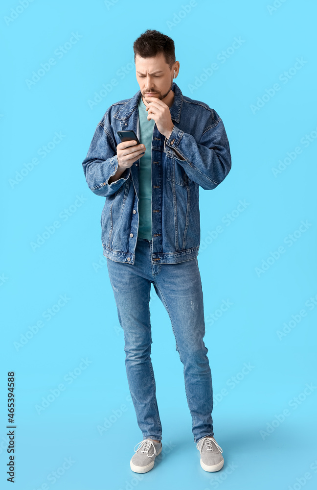 Frowning man with phone and earphones on color background