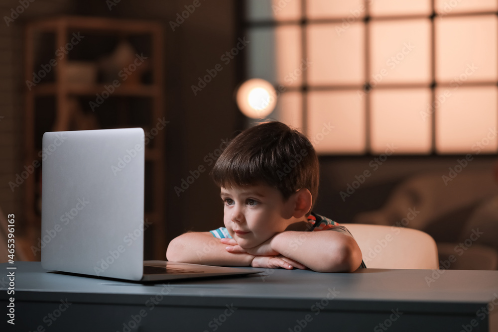 Little boy watching cartoons on laptop at table late in evening